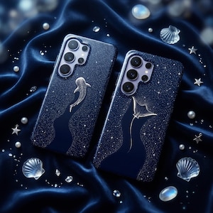 Op de afbeelding: Twee marineblauwe telefoonhoesjes met een sterrenhemelontwerp. Eén hoesje heeft een walvishaai, de andere een manta rog. De hoesjes zijn omgeven door parels, schelpen en stervormige decoraties op een donkerblauwe fluwelen stof.