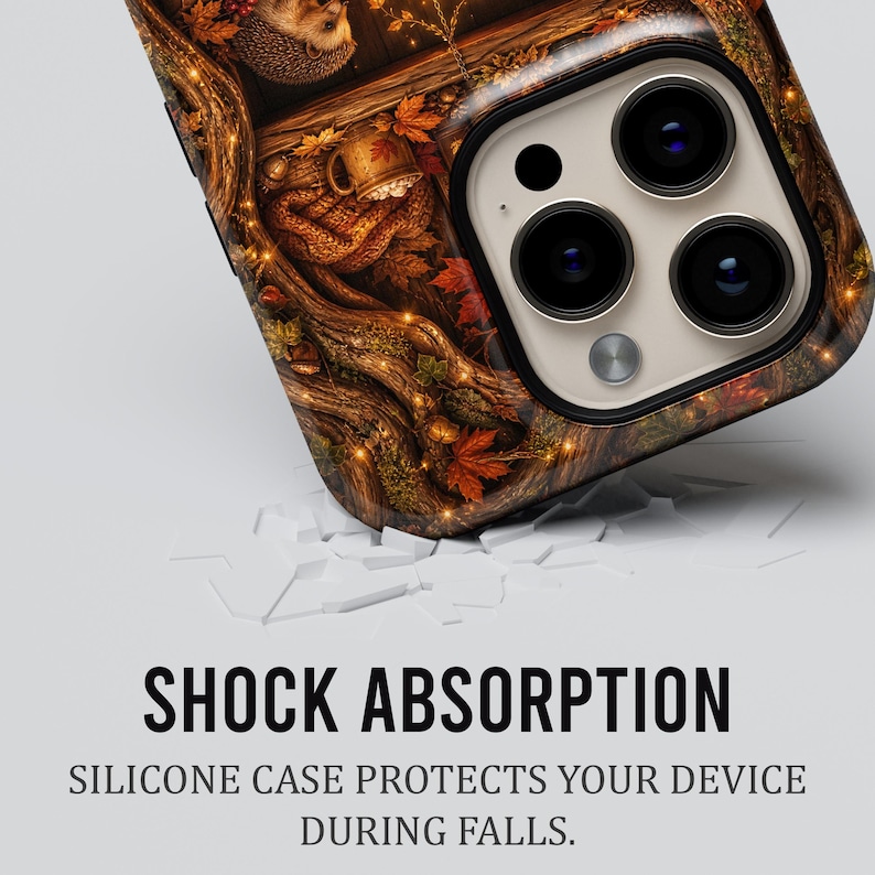 May include: A smartphone case featuring a detailed autumn forest scene with a hedgehog, fallen leaves, and a mug. The text SHOCK ABSORPTION and SILICONE CASE PROTECTS YOUR DEVICE DURING FALLS is printed below the case on a plain white background.