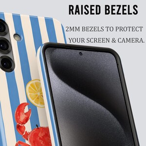 May include: A phone case with a blue and white striped pattern, a lemon slice, and a red crab illustration. The case has raised bezels for screen and camera protection. Text on the image reads: "RAISED BEZELS" and "2MM BEZELS TO PROTECT YOUR SCREEN & CAMERA."