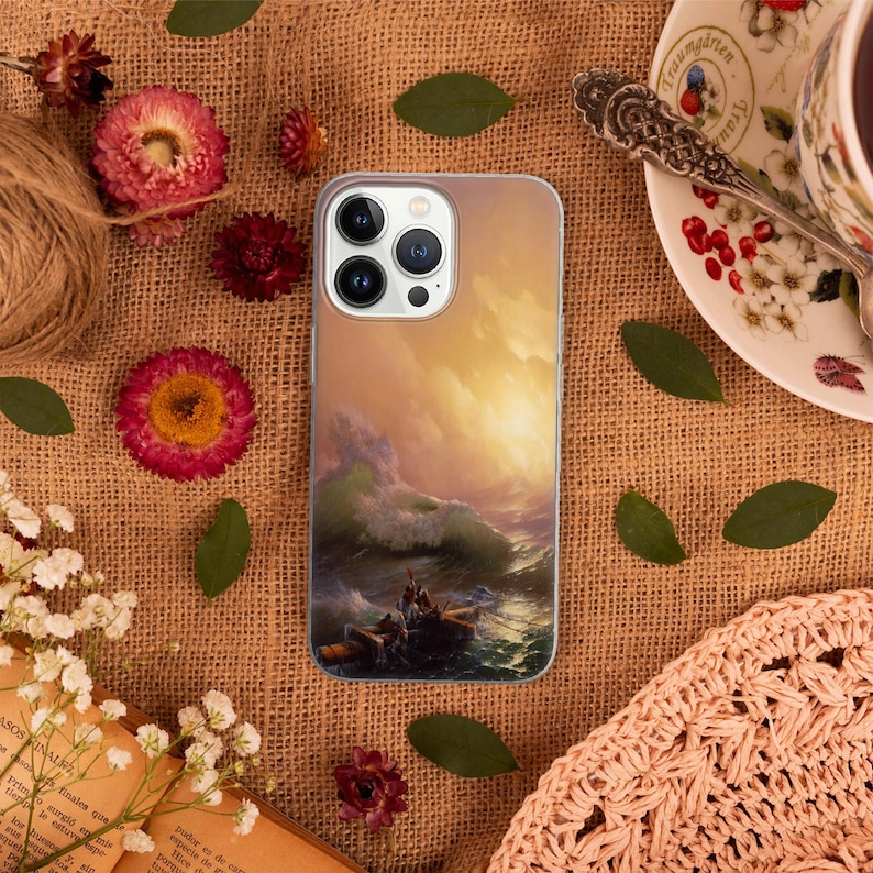 Peut inclure: Une coque de t&eacute;l&eacute;phone avec une peinture d'une mer orageuse avec un bateau et des personnes &agrave; l'int&eacute;rieur. Le ciel est d'un orange et d'un jaune vif. La coque de t&eacute;l&eacute;phone est blanche et a une d&eacute;coupe pour l'objectif de l'appareil photo.