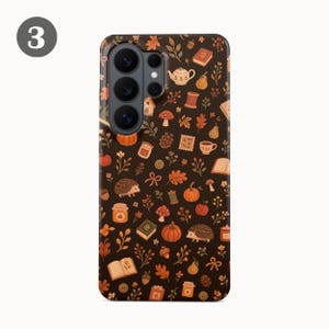 Puede incluir: Una funda de smartphone marr&oacute;n oscuro con un patr&oacute;n repetitivo de ilustraciones en naranja y crema que incluyen erizos, calabazas, setas, libros, teteras, tarros, hojas, bellotas, botones y carretes de hilo sobre toda la superficie.