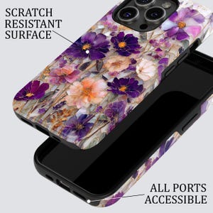 May include: A phone case with a floral design featuring purple, pink, and orange flowers. The case has a scratch-resistant surface and all ports are accessible. The text "SCRATCH RESISTANT SURFACE" and "ALL PORTS ACCESSIBLE" are visible.