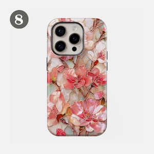 May include: A phone case featuring a floral design with pink and white blossoms. The case has a glossy finish and a raised design, with a light background. The case has a camera cutout and buttons.