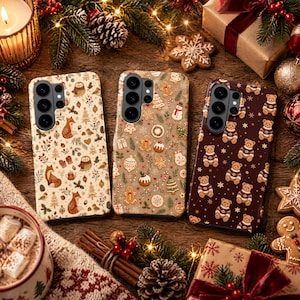 May include: Three smartphone cases featuring festive patterns. The left case has foxes and owls on a cream background. The middle case displays gingerbread cookies and holiday treats on a tan background. The right case shows teddy bears on brown.