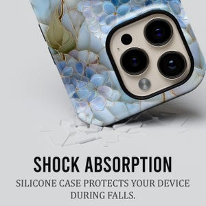 May include: A smartphone case with a floral design in shades of blue and gold. The case features a close-up of the camera lenses. The text "SHOCK ABSORPTION" and "SILICONE CASE PROTECTS YOUR DEVICE DURING FALLS" is displayed.