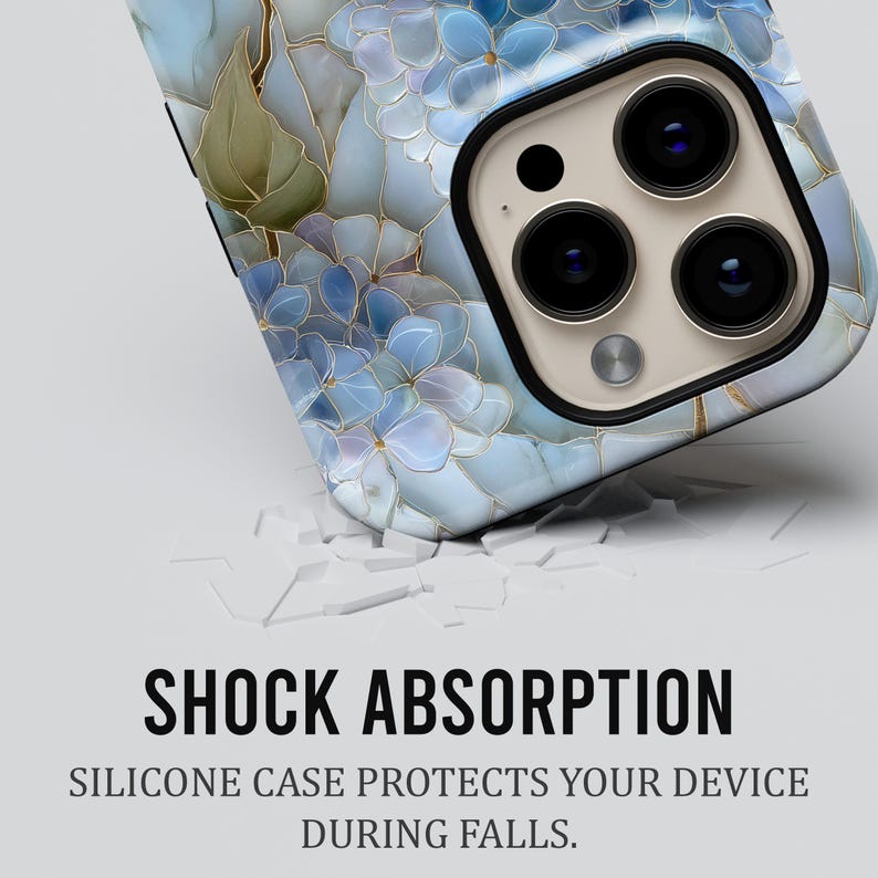 May include: A smartphone case with a floral design in shades of blue and gold. The case features a close-up of the camera lenses. The text "SHOCK ABSORPTION" and "SILICONE CASE PROTECTS YOUR DEVICE DURING FALLS" is displayed.