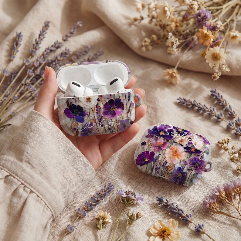 May include: AirPods Pro case with a floral design featuring purple and orange flowers. The case is open, revealing white AirPods. The case has the name "Charlotte" written on it in cursive.