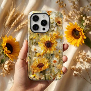 May include: A floral phone case featuring a vibrant design of yellow sunflowers and white daisies. The case has a glossy finish and a detailed, artistic rendering of the flowers. The background is a soft, neutral color, enhancing the bright floral pattern.