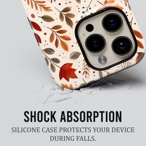 Puede incluir: Una funda para smartphone con fondo crema que presenta un patr&oacute;n de hojas de oto&ntilde;o marrones, naranjas y rojas y peque&ntilde;os puntos negros. El texto SHOCK ABSORPTION y SILICONE CASE PROTECTS YOUR DEVICE DURING FALLS aparece impreso debajo.