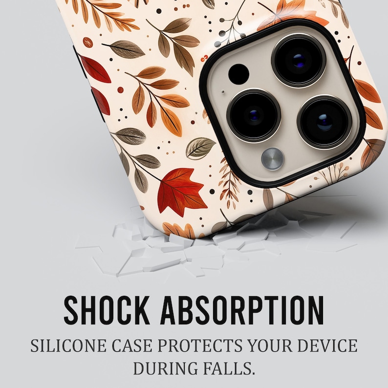 Puede incluir: Una funda para smartphone con fondo crema que presenta un patr&oacute;n de hojas de oto&ntilde;o marrones, naranjas y rojas y peque&ntilde;os puntos negros. El texto SHOCK ABSORPTION y SILICONE CASE PROTECTS YOUR DEVICE DURING FALLS aparece impreso debajo.