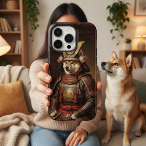 Peut inclure: Une coque de téléphone avec un Shiba Inu en armure de samouraï. L'étui a un fond sombre avec le portrait du chien au centre. Le chien porte un casque et une armure japonais traditionnels avec des accents rouges et dorés. Un vrai Shiba Inu est à côté.