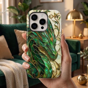 May include: A smartphone case featuring a detailed illustration of a green dragon with intricate gold-toned linework. The design mimics a stained glass aesthetic with layered scales and swirling patterns set against a cream-coloured background.