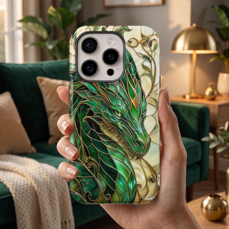 May include: A smartphone case featuring a detailed illustration of a green dragon with intricate gold-toned linework. The design mimics a stained glass aesthetic with layered scales and swirling patterns set against a cream-coloured background.