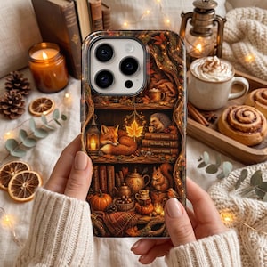 May include: A smartphone case featuring a detailed autumn-themed illustration of a cozy bookshelf. The design includes a sleeping fox, a hedgehog, a squirrel, pumpkins, books titled Harvest Stories, The Reading Nook, and Tales of Wonder.