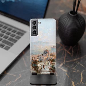 May include: A clear phone case with a colorful painting of a cityscape with a church building in the center. The case has a camera cutout on the back.