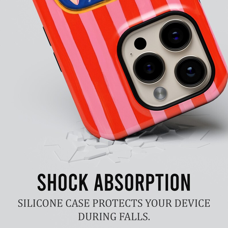 May include: A close-up of a phone case with a red and pink striped pattern. The phone case has a black border and three camera lenses. The text "SHOCK ABSORPTION" and "SILICONE CASE PROTECTS YOUR DEVICE DURING FALLS" is visible.