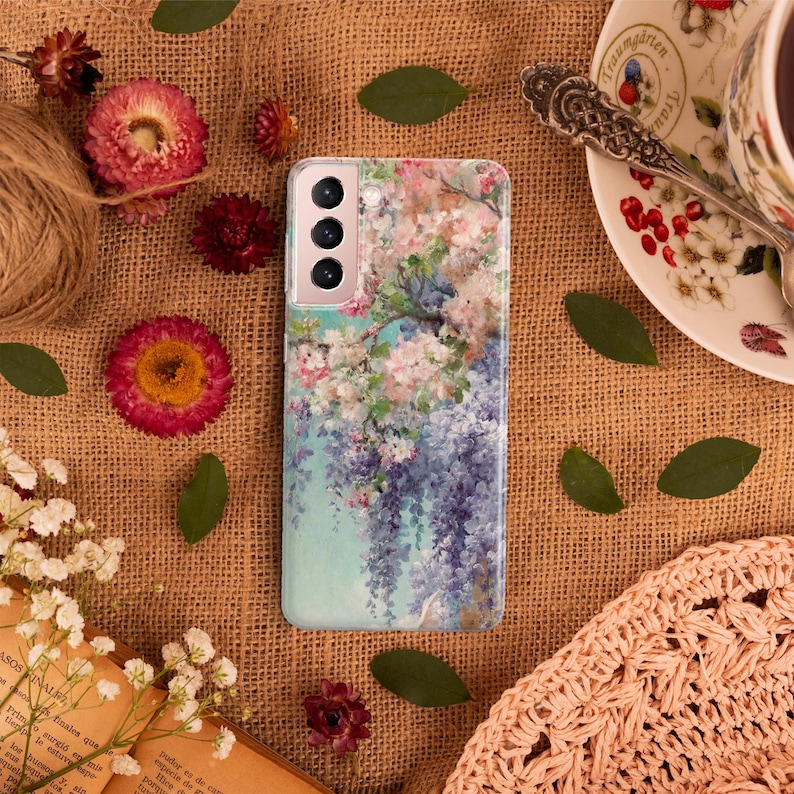 May include: A phone case with a floral design featuring pink and purple flowers on a blue background. The case has a camera cutout with three lenses.