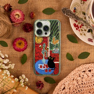 K&ouml;nnte beinhalten: Eine Handyh&uuml;lle mit einem farbenfrohen abstrakten Design, das eine schwarze Katze, rote &Auml;pfel und eine Vase mit Blumen zeigt. Die H&uuml;lle hat einen Ausschnitt f&uuml;r das Kameraobjektiv und der Text "HENRI MATISSE" ist unten aufgedruckt.