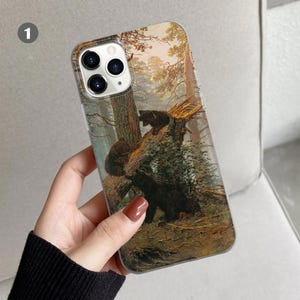 Peut inclure: Une coque de t&eacute;l&eacute;phone avec une image color&eacute;e d'ours dans une for&ecirc;t. La coque a un dos transparent et une bordure blanche. L'image est une peinture d'une sc&egrave;ne de for&ecirc;t avec trois ours. Les ours sont bruns et noirs et se tiennent sur une branche d'arbre. La for&ecirc;t est verte et brune et a beaucoup d'arbres. La coque est con&ccedil;ue pour s'adapter &agrave; un t&eacute;l&eacute;phone avec un objectif d'appareil photo &agrave; l'arri&egrave;re.
