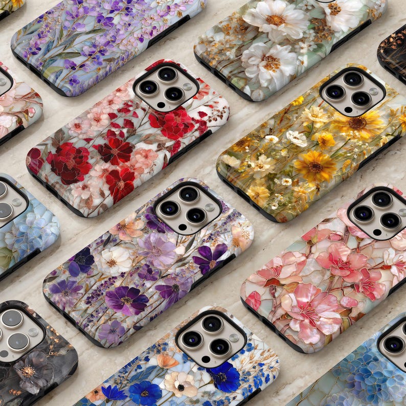 May include: A collection of floral-patterned phone cases. The cases feature various flower designs in shades of red, pink, yellow, purple, and white. The cases are arranged on a light-colored surface, showcasing the intricate floral patterns.