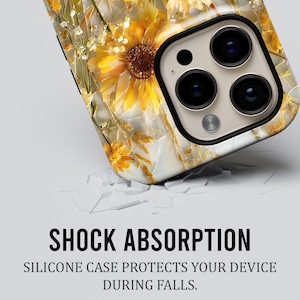 May include: A phone case with a floral design featuring sunflowers and other yellow and gold flowers. The case has a white background and a black border around the camera lenses. The text "SHOCK ABSORPTION" is visible.