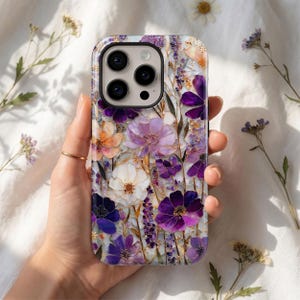 May include: A floral phone case featuring a vibrant design of purple, white, and orange flowers. The case has a glossy finish and a protective design. The flowers are arranged in a detailed, artistic pattern, creating a stylish accessory.