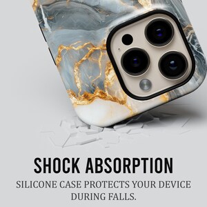 May include: A white phone case with a blue and gold marble design. The case is cracked, suggesting it has been dropped. The text "SHOCK ABSORPTION" and "SILICONE CASE PROTECTS YOUR DEVICE DURING FALLS." is displayed below the case.