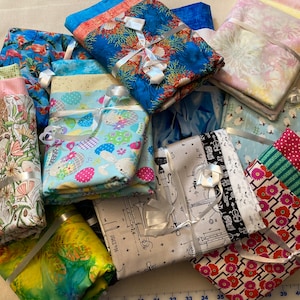 May include: A collection of fabric squares, each with a different pattern and color, tied with white ribbon. The fabrics include floral, geometric, and musical note designs.