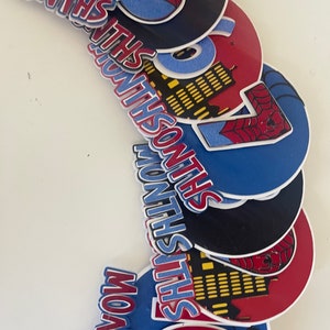 Puede incluir: Colecci&oacute;n de recortes coloridos en capas con el texto "MONTHS" y n&uacute;meros. Los recortes son rojos, azules y negros, con un tema de Spider-Man. Algunos recortes tienen dise&ntilde;os de horizonte y telara&ntilde;a.
