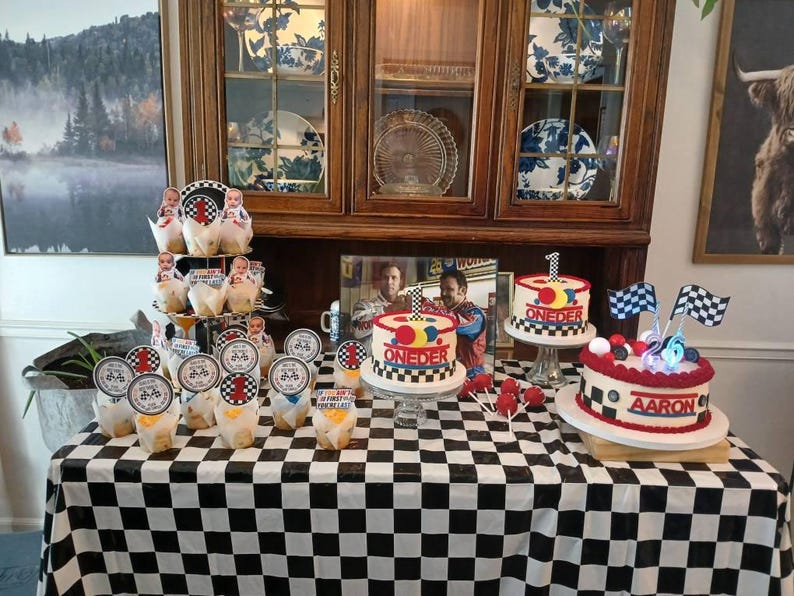May include: A birthday party table with a black and white checkered tablecloth. The table is decorated with cupcakes, cake pops, and three cakes. The cakes are decorated with racing flags and the word "ONEDER" and "Aaron".