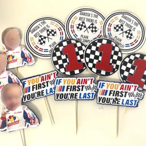 May include: A collection of racing-themed party decorations. Includes circular toppers with checkered flags and the text "Dakota's the best there is" and "1". Also, cutouts of race car drivers and signs that read "If you ain't first you're last".