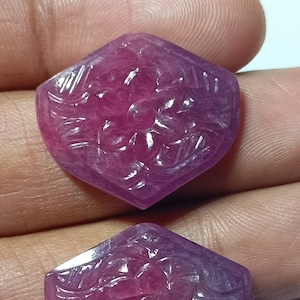 May include: Two carved gemstone pendants in a hexagonal shape. The gemstones are a gradient of pink to purple, with a floral design carved into the surface. The pendants are displayed against a neutral background.