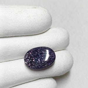 May include: A close-up of a purple and silver oval gemstone with a sparkly finish.