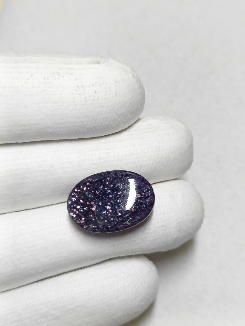 May include: A close-up of a purple and silver oval gemstone with a sparkly finish.