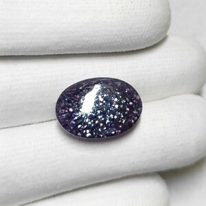 May include: A close-up of a purple and silver oval gemstone with a sparkly, iridescent finish.