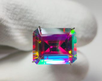 May include: A vibrant, iridescent gemstone with a rectangular shape and a deep purple hue. The gemstone is set in a prong setting and is surrounded by a rainbow of colors.