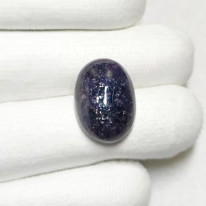 May include: A dark purple oval gemstone with a sparkly, iridescent finish. The gemstone is set in a white, oval-shaped setting.