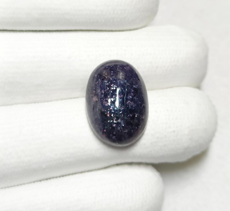 May include: A dark purple oval gemstone with a sparkly, iridescent finish. The gemstone is set in a white, oval-shaped setting.