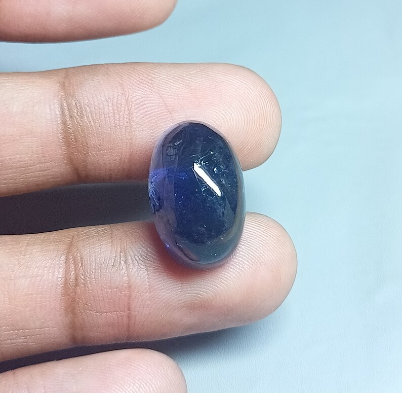 May include: A dark blue oval-shaped gemstone with a slight purple hue.