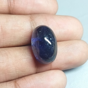 May include: A dark blue oval-shaped gemstone with a slight purple hue. The gemstone is smooth and polished.