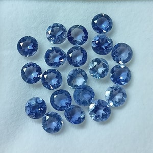 May include: A collection of round, blue gemstones, likely sapphires, displayed on a white surface. The gemstones are various sizes and shades of blue.