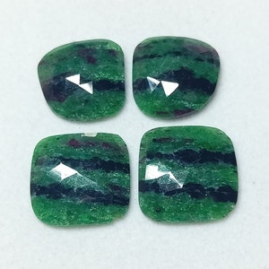 Puede incluir: Cuatro cabujones de piedras preciosas verdes, negras y rosas con un corte facetado. Las piedras preciosas están engastadas en forma de cojín.