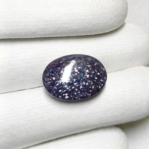 May include: A close-up of a purple and silver oval gemstone with a sparkly, iridescent finish.