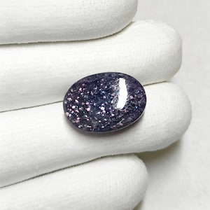 May include: A close-up of a purple and white oval gemstone with a sparkly, iridescent finish.