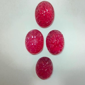 Può includere: Quattro pietre preziose ovali scolpite in una vibrante tonalità rossa. Ogni gemma presenta un elaborato motivo floreale. Le pietre sono disposte a forma di diamante su sfondo bianco.