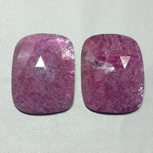 Pode incluir: Dois cabochões de pedra preciosa rosa com uma faceta triangular no centro. As pedras preciosas são cortadas em forma de almofada e têm uma superfície lisa e polida.