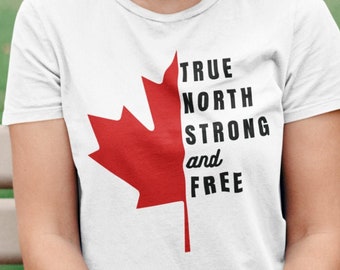 May include: A woman wearing a white t-shirt with a red maple leaf and the text "TRUE NORTH STRONG and FREE". She is sitting on a wooden bench and holding a bouquet of orange flowers.