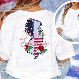 May include: White t-shirt featuring a graphic of the New Jersey state outline, incorporating the American flag design. The text "New Jersey" is written in a cursive font. Floral accents in red, white, and blue are included.