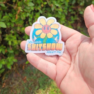 K&ouml;nnte beinhalten: Ein wei&szlig;er Aufkleber mit einer gelben Blume mit einem l&auml;chelnden Gesicht und dem Text "Welcome to the SHITSOW Enjoy your stay!"