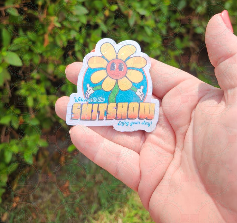 K&ouml;nnte beinhalten: Ein wei&szlig;er Aufkleber mit einer gelben Blume mit einem l&auml;chelnden Gesicht und dem Text "Welcome to the SHITSOW Enjoy your stay!"